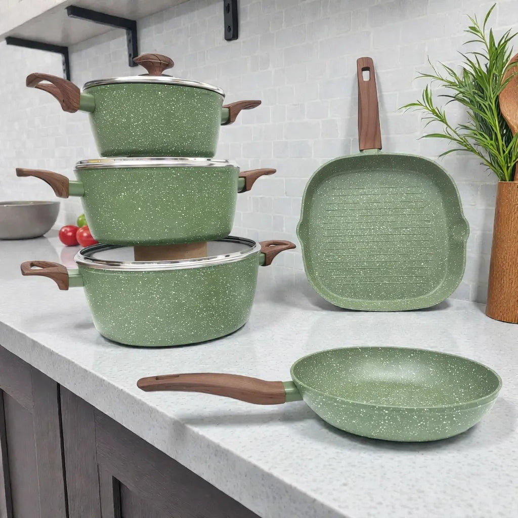 Set de ollas Epicure by Joseph Marcus Olive Collection color verde oliva con recubrimiento antiadherente, tres ollas con tapa de vidrio, sartén redondo y sartén parrilla cuadrado, foto lifestyle sobre encimera de cocina.