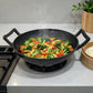 Wok de hierro fundido epicure by Joseph Marcus negro 31 cm sobre estufa, cocinando vegetales salteados con vapor visible, con dos asas laterales.