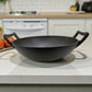 Wok de hierro fundido Epicure by Joseph Marcus negro 31 cm sobre encimera, foto en ambiente de cocina con fondo desenfocado y dos asas laterales.