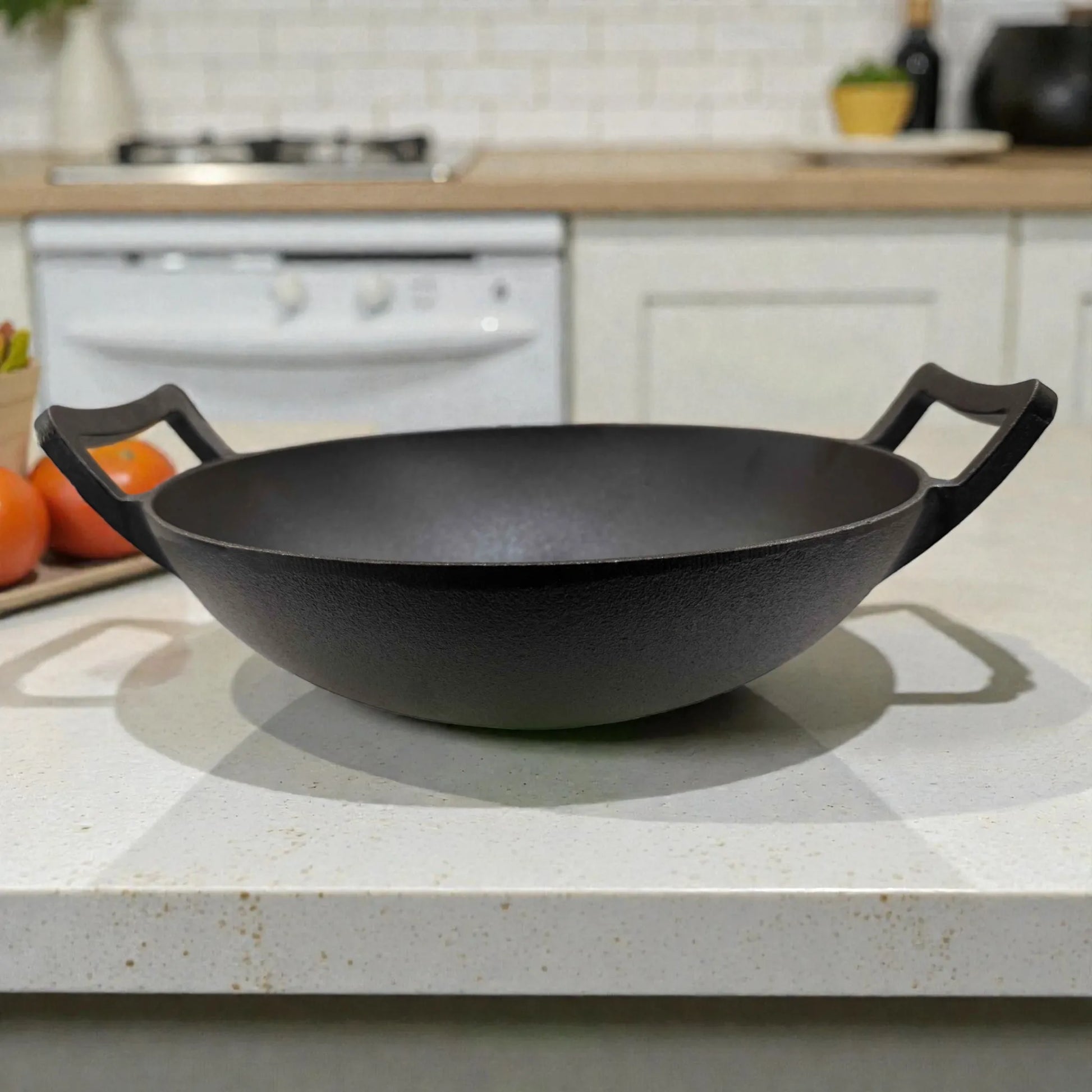 Wok de hierro fundido Epicure by Joseph Marcus negro 31 cm sobre encimera, foto en ambiente de cocina con fondo desenfocado y dos asas laterales.