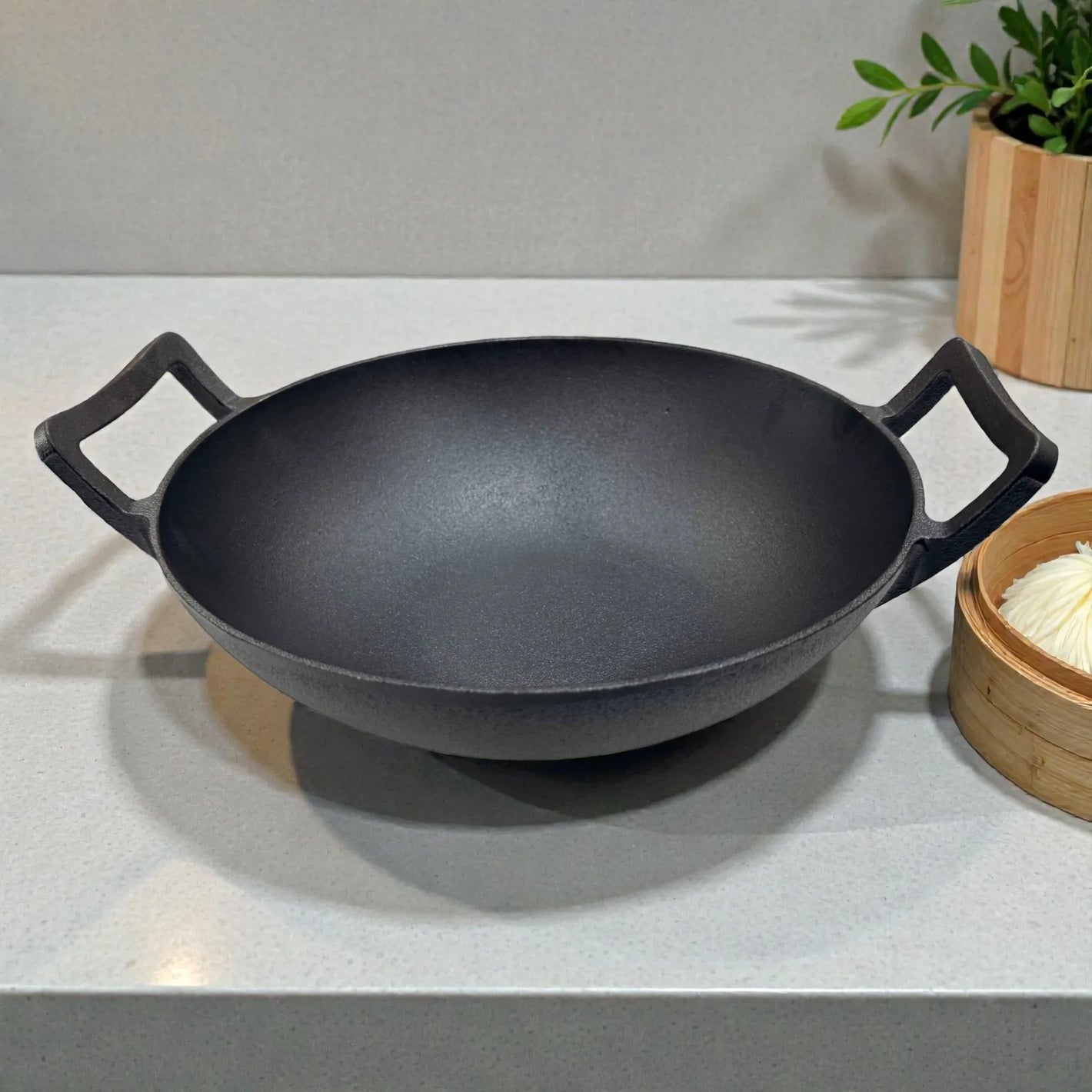 Wok de hierro fundido epicure by Joseph Marcus color negro de 31 cm, vista frontal con dos asas, colocado sobre encimera de cocina.