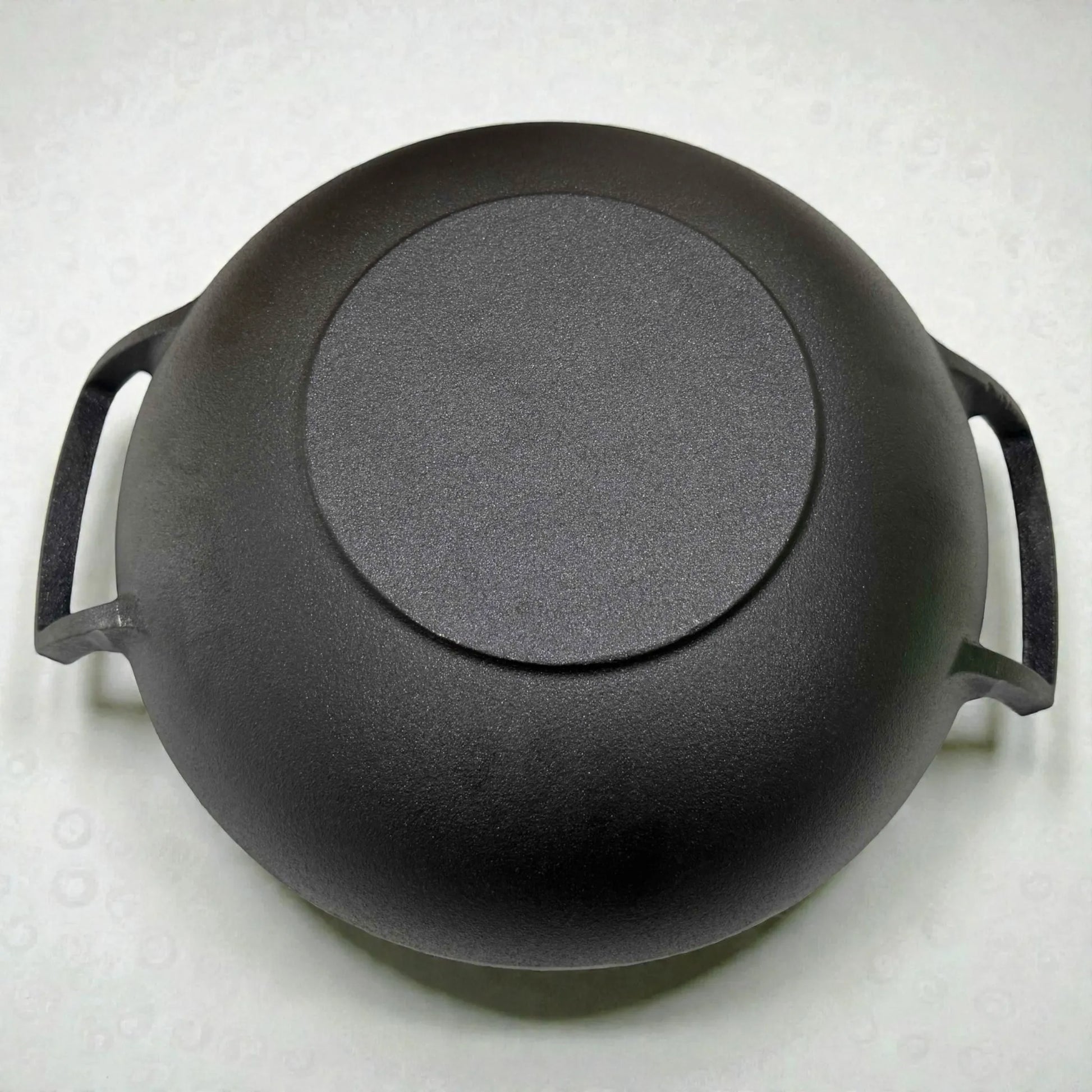 Parte inferior del wok de hierro fundido Epicure by Joseph Marcus negro 31 cm, mostrando la base circular y las asas laterales.