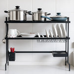 Vista frontal del escurridor de platos MISOL de dos niveles, acero color negro, tamaño 84×30×75 cm; nivel superior con ollas y sartén, nivel inferior con porta platos ondulado, canastilla metálica, porta cubiertos y bandeja lateral, instalado sobre el fregadero en cocina moderna.