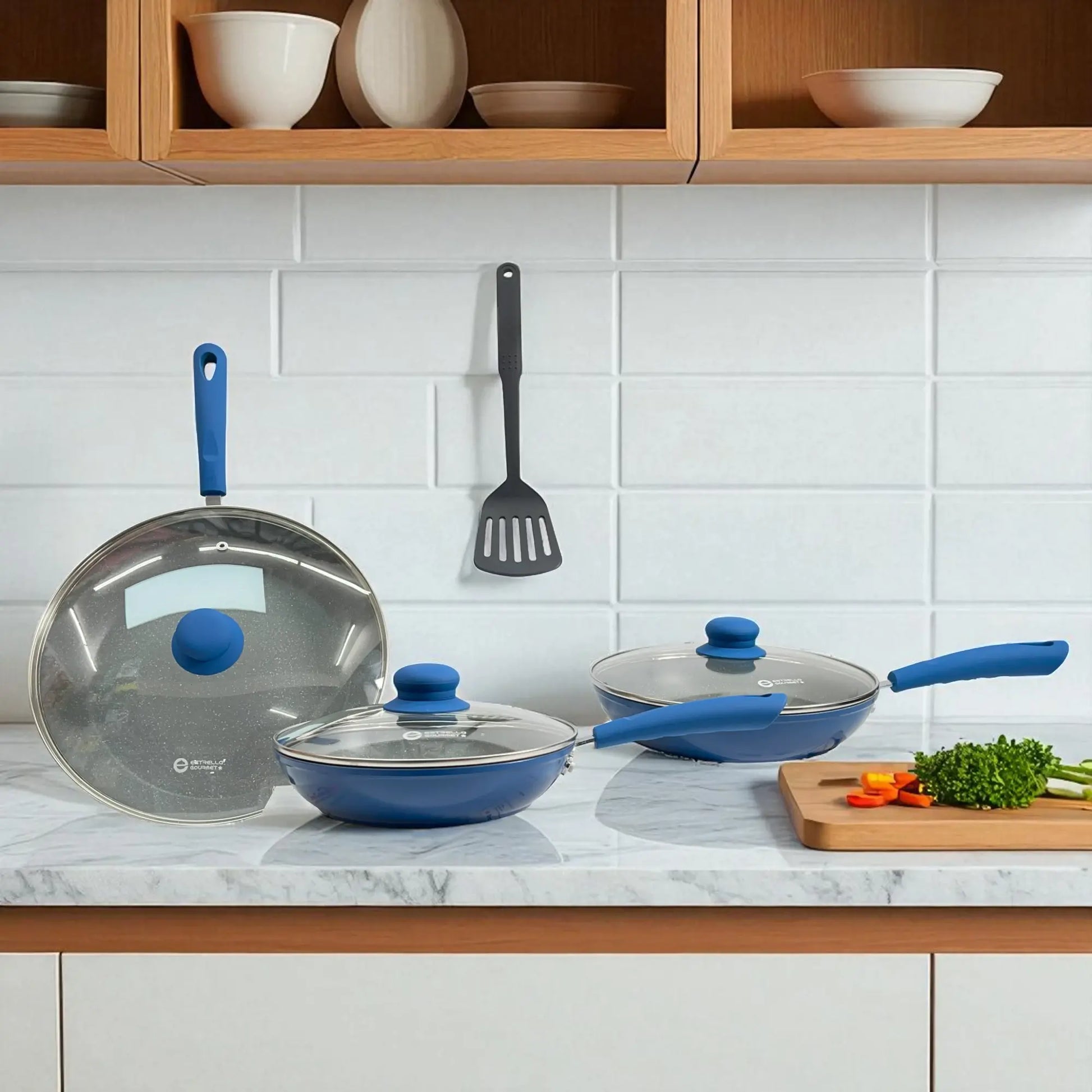 Vista frontal del set Estrella Gourmet azul con tres sartenes de la línea marmolizada, cada uno con tapa de vidrio y mango ergonómico.