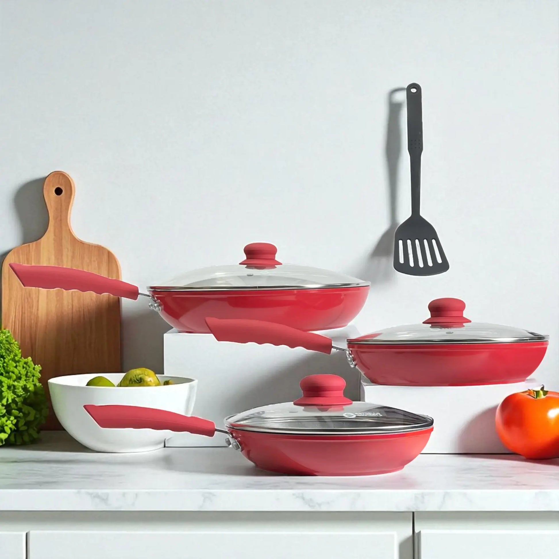 Set Estrella Gourmet línea marmolizada en rojo con tres sartenes 20, 24 y 30 cm, tapas de vidrio y espátula colgada, composición lateral sobre encimera.
