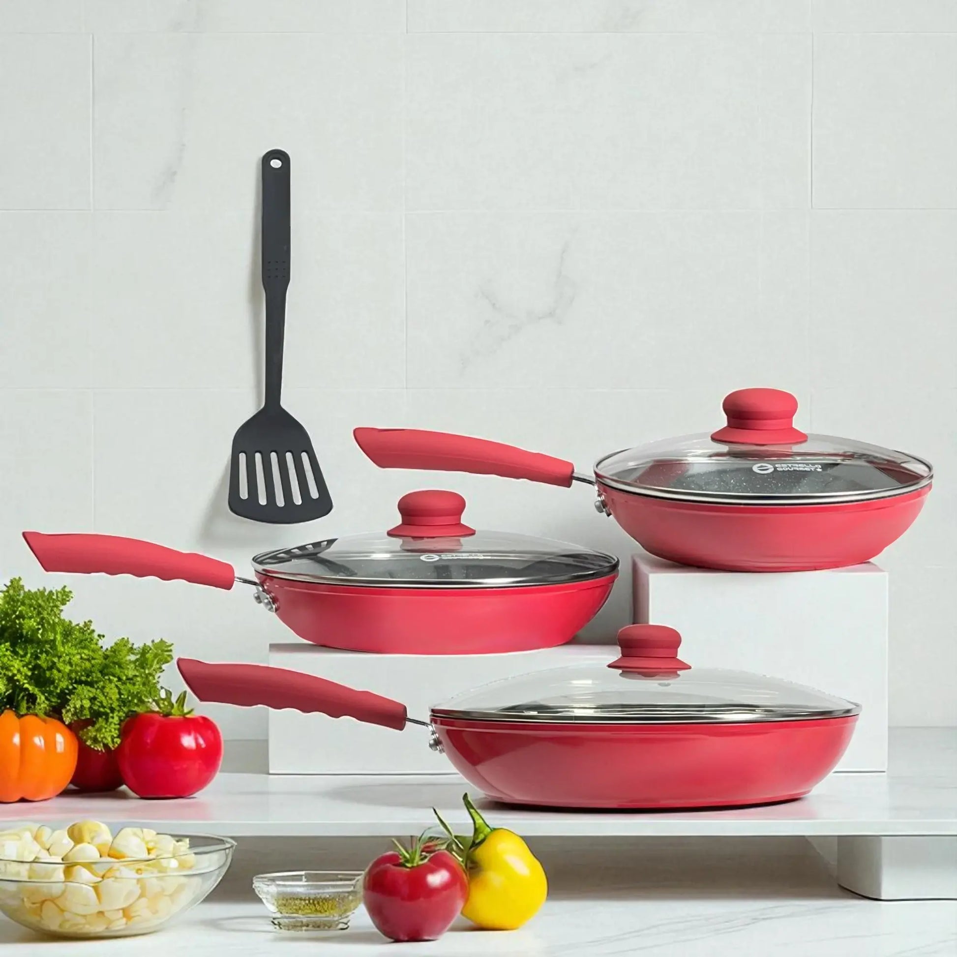Juego de sartenes Estrella Gourmet rojo, 7 piezas con tres tapas de vidrio y espátula de nylon, tamaños 20, 24 y 30 cm, vista frontal en cocina.