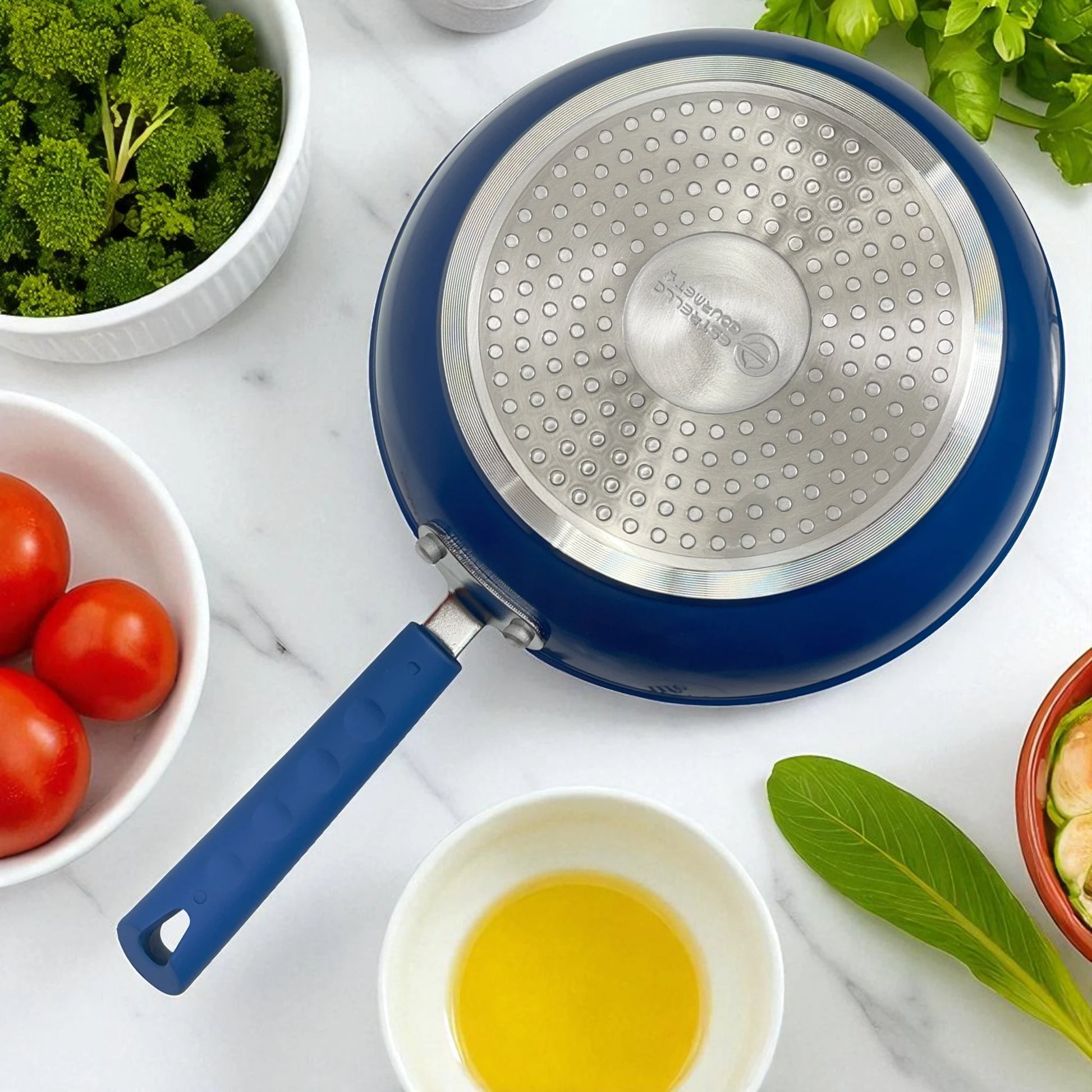 Detalle inferior del sartén Estrella Gourmet color azul con disco de acero inoxidable para inducción y mango de baquelita; línea marmolizada, válido para 20, 24 y 30 cm.