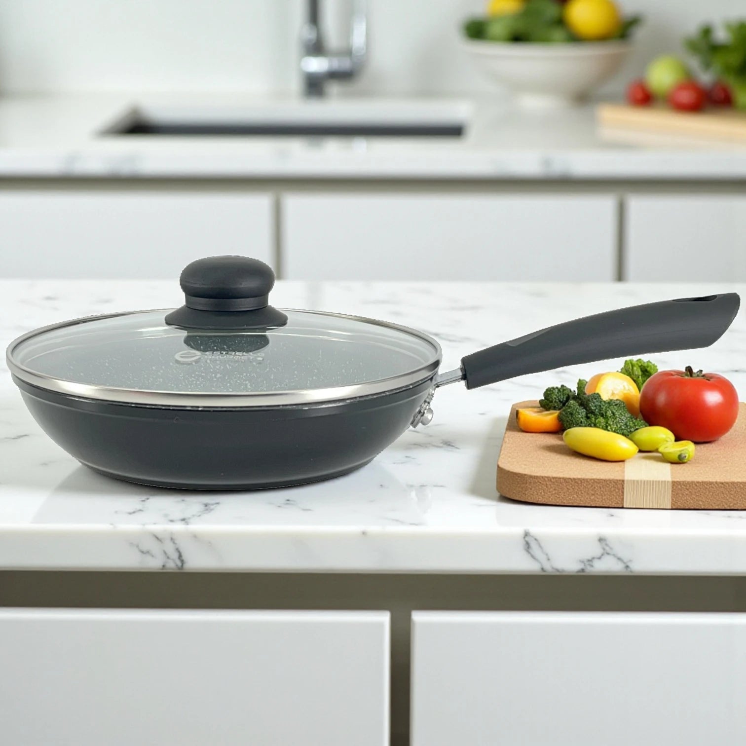 Sartén Estrella Gourmet con tapa de vidrio, exterior negro e interior marmolizado sobre encimera de cocina junto a tabla con verduras; disponible en 20, 24 y 30 cm.