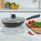 Sartén Estrella Gourmet con tapa de vidrio, interior gris marmolizado y mango de baquelita a la derecha sobre encimera de mármol; verduras y chiles a un lado, tamaños disponibles 20, 24 y 30 cm.