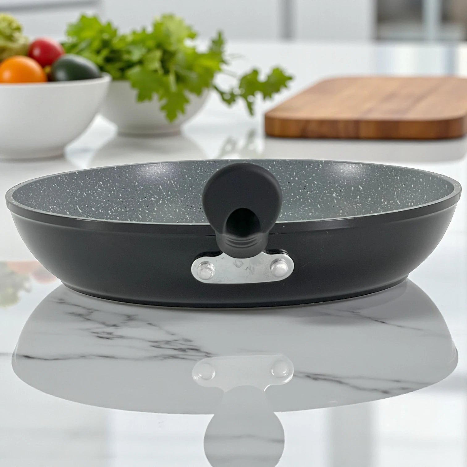 Detalle de remaches de unión del mango de baquelita y pico vertedor en sartén con interior marmolizado gris.