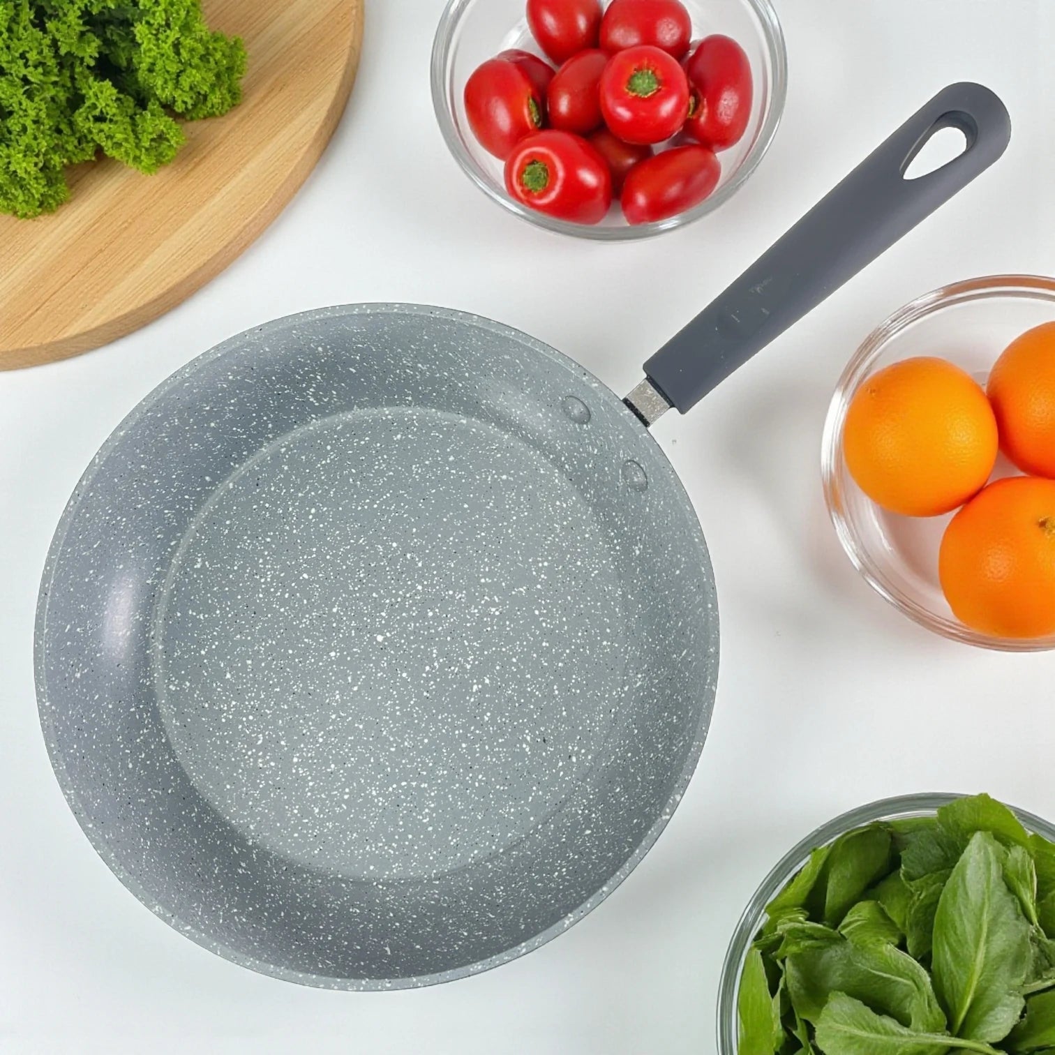 Vista superior del sartén Estrella Gourmet que muestra el antiadherente marmolizado gris de 3 capas y el mango de baquelita; ingredientes alrededor, disponible en 20, 24 y 30 cm.