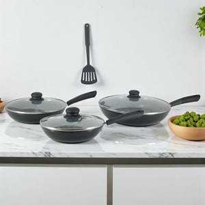 Tres sartenes de 20, 24 y 30 cm con tapas de vidrio y mangos de baquelita, espátula colgada y disposición alineada sobre encimera.