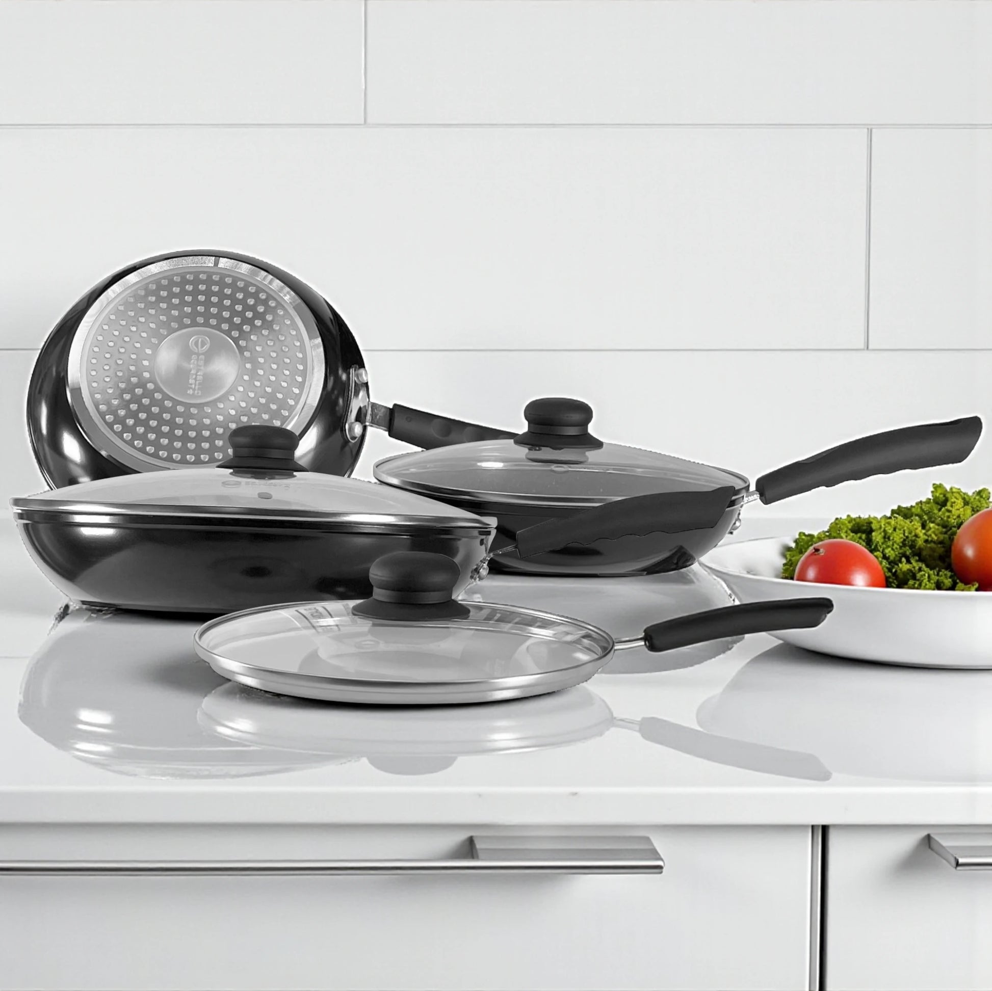 Detalle del fondo con disco para inducción en acero inoxidable del sartén Estrella Gourmet, junto a sartenes con tapas de vidrio.