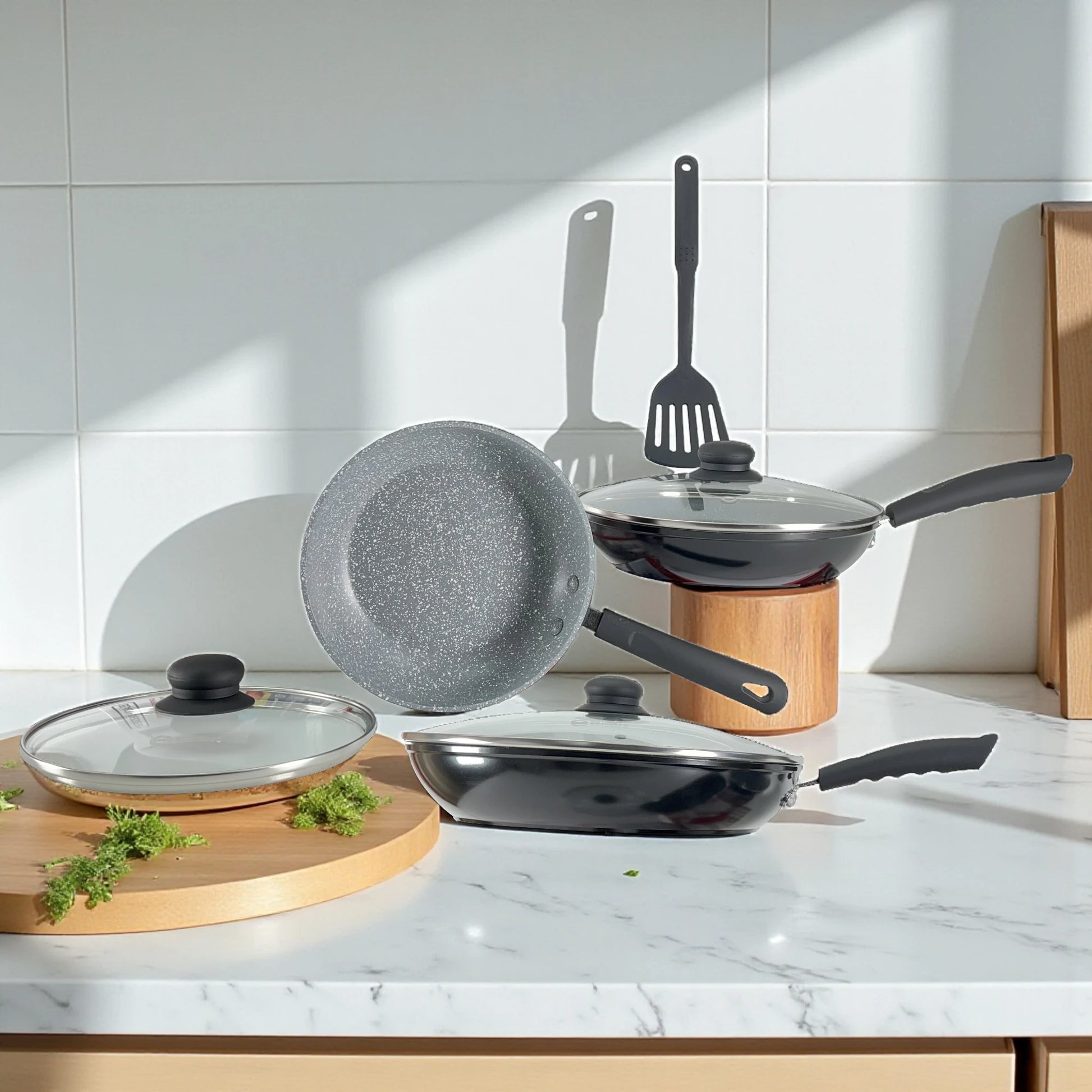 Composición con luz natural mostrando el interior gris marmolizado del sartén pequeño, más dos sartenes con tapa de vidrio.