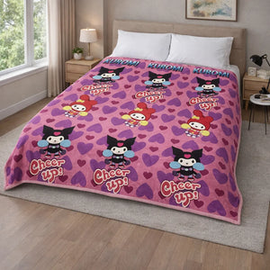Frazada piel de borrego infantil Kuromi (Sanrio) color morado con corazones, 230x190 cm y 1500 g, colocada sobre cama; estampado con Kuromi y texto decorativo “Cheer up!”.