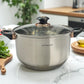 Cacerola grande Hoffavorer de 24 cm (6.6 L) en acero inoxidable 18/10, color plateado con tapas de vidrio y perilla negra con aro dorado, dos asas negras; sobre encimera de cocina.