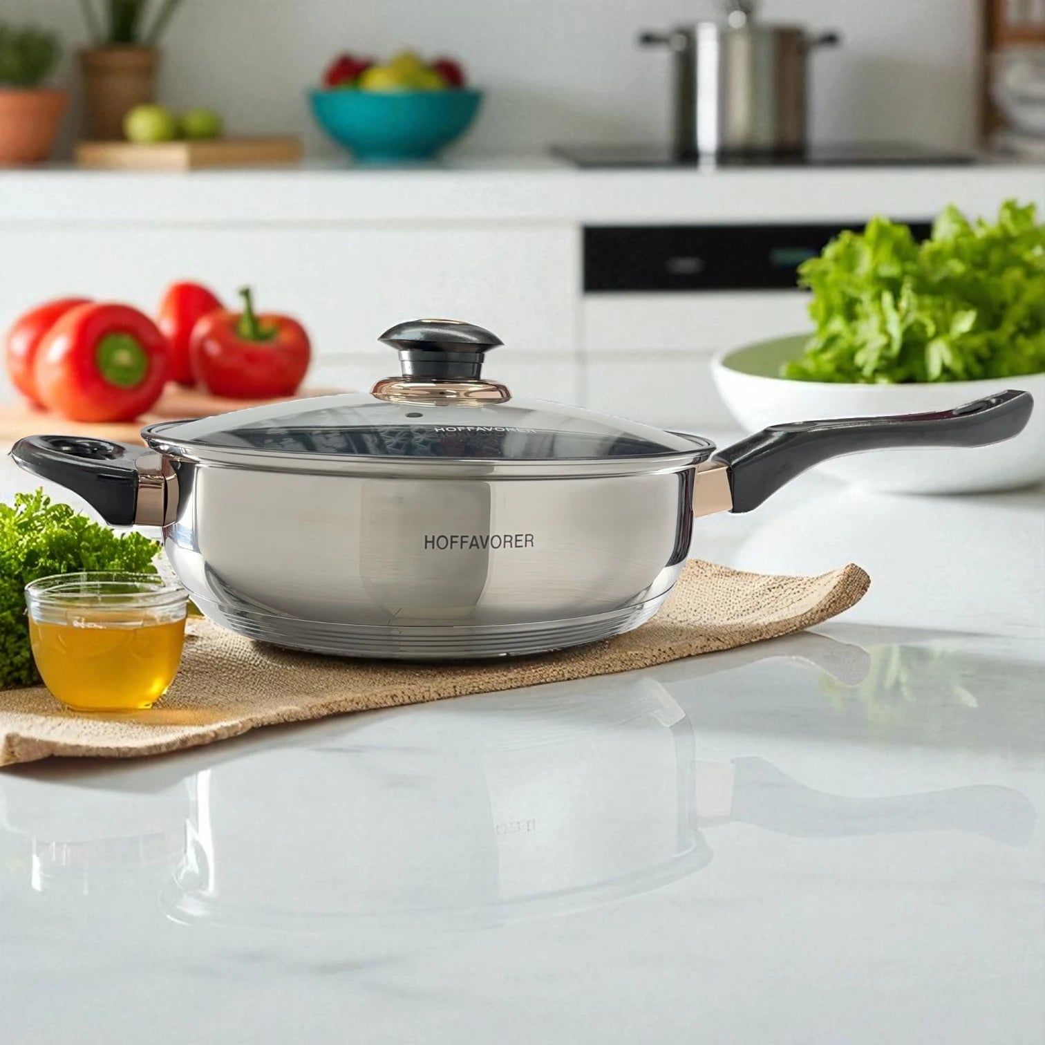 Sartén Hoffavorer de 24 cm (3.4 L) en acero inoxidable 18-10 con recubrimiento antiadherente Xylan Plus, tapa de vidrio, mango largo negro y asa auxiliar; vista lateral sobre encimera de cocina.