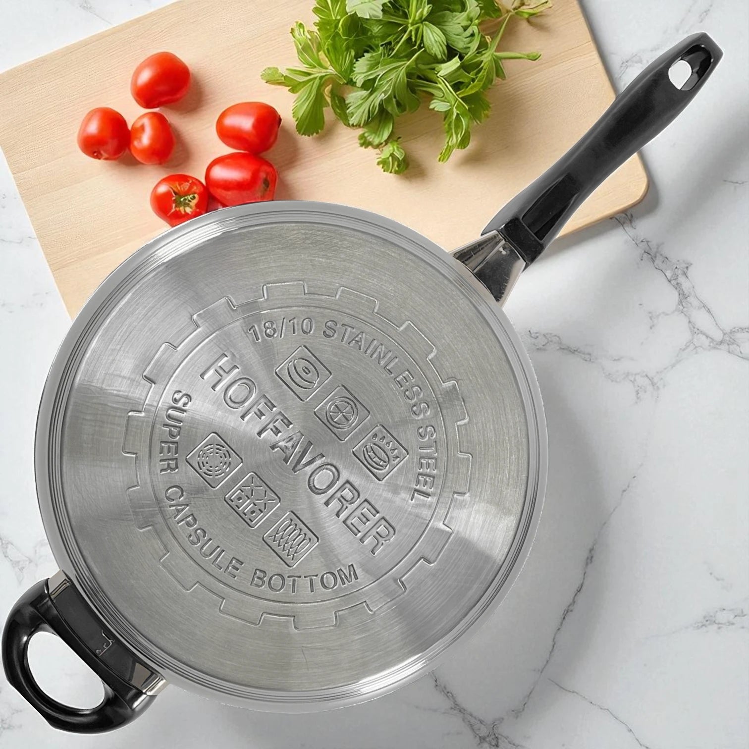 Vista superior del fondo capsulado del sartén Hoffavorer 24 cm con sello Super Capsule Bottom en acero 18-10, compatible con inducción, mango negro y asa auxiliar; encimera marmoleada con tomates y hierbas.