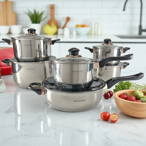 Set Hoffavorer HF-4441 de 12 piezas en acero inoxidable plateado; en primer plano sartén 24 cm con tapa y cazo 16 cm encima, al fondo cacerolas 18, 20 y 24 cm con tapas de vidrio, asas negras y detalles dorados; encimera blanca.