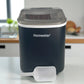 Máquina de hielo Homestar HS-Z6Y1B color negro, vista frontal con tapa cerrada y pala blanca frente al equipo en una encimera de cocina.