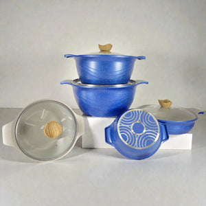 Composición del set HotChef de ollas granito color azul jaspeado con tapas de vidrio y perilla tipo madera; dos ollas apiladas al centro, una cacerola baja a la derecha y tapa de vidrio vista frontal a la izquierda sobre fondo blanco.