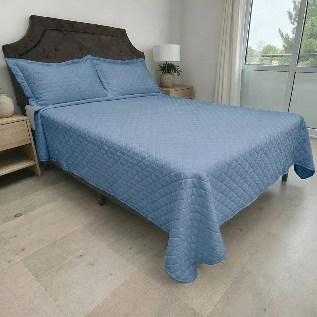 Cubrecama HPC Polo color azul acero sobre cama, vista lateral derecha en dormitorio con ventana y fundas de almohada a juego.