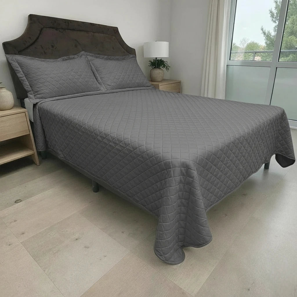 Cubrecama HPC Polo color gris sobre cama, vista lateral derecha en dormitorio con ventana y fundas de almohada a juego.