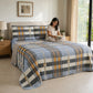 Mujer leyendo sobre una cama con cubrecama reversible de cuadros azul, gris y mostaza.
