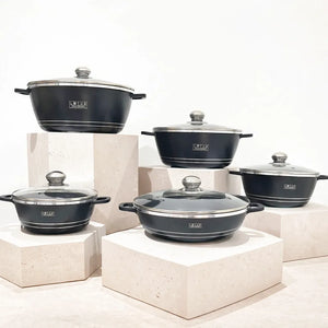 Juego de ollas Lotus Home Collection color negro en aluminio fundido con tapas de vidrio, vista frontal del set sobre bases decorativas.