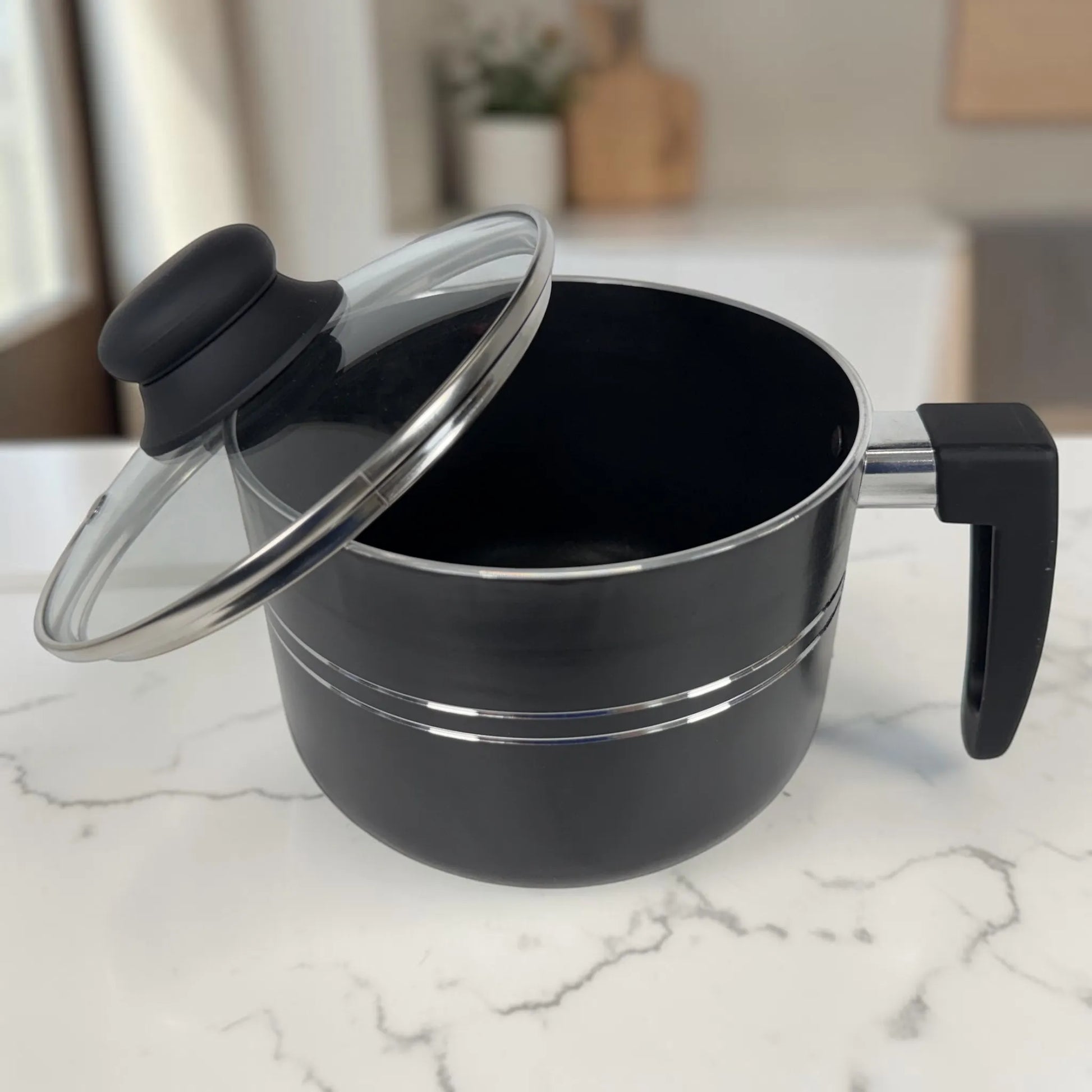 Lechero ROCA negro antiadherente con tapa de vidrio abierta y mango ergonómico, parte del juego de ollas de 12 piezas.