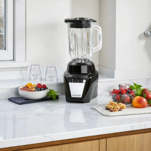 Licuadora Black+Decker BL08764BDLA negra con jarra de vidrio sobre encimera de cocina moderna, acompañada de frutas, nueces y recipientes, ideal para batidos, jugos y smoothies.