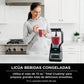 Licuadora Ninja Professional Plus BN701 sobre encimera de cocina moderna junto a una mujer sosteniendo un vaso de smoothie rojo, mostrando su uso para bebidas congeladas.