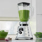 Licuadora clásica Oster cromada BLST4655 con batido verde en vaso de vidrio, ubicada en cocina moderna.