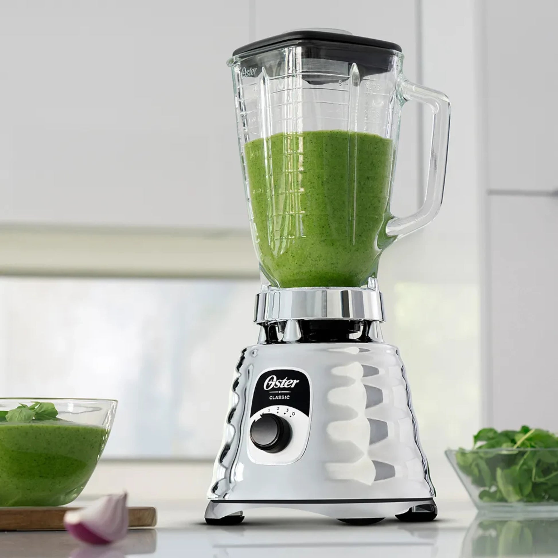 Licuadora clásica Oster cromada BLST4655 con batido verde en vaso de vidrio, ubicada en cocina moderna.