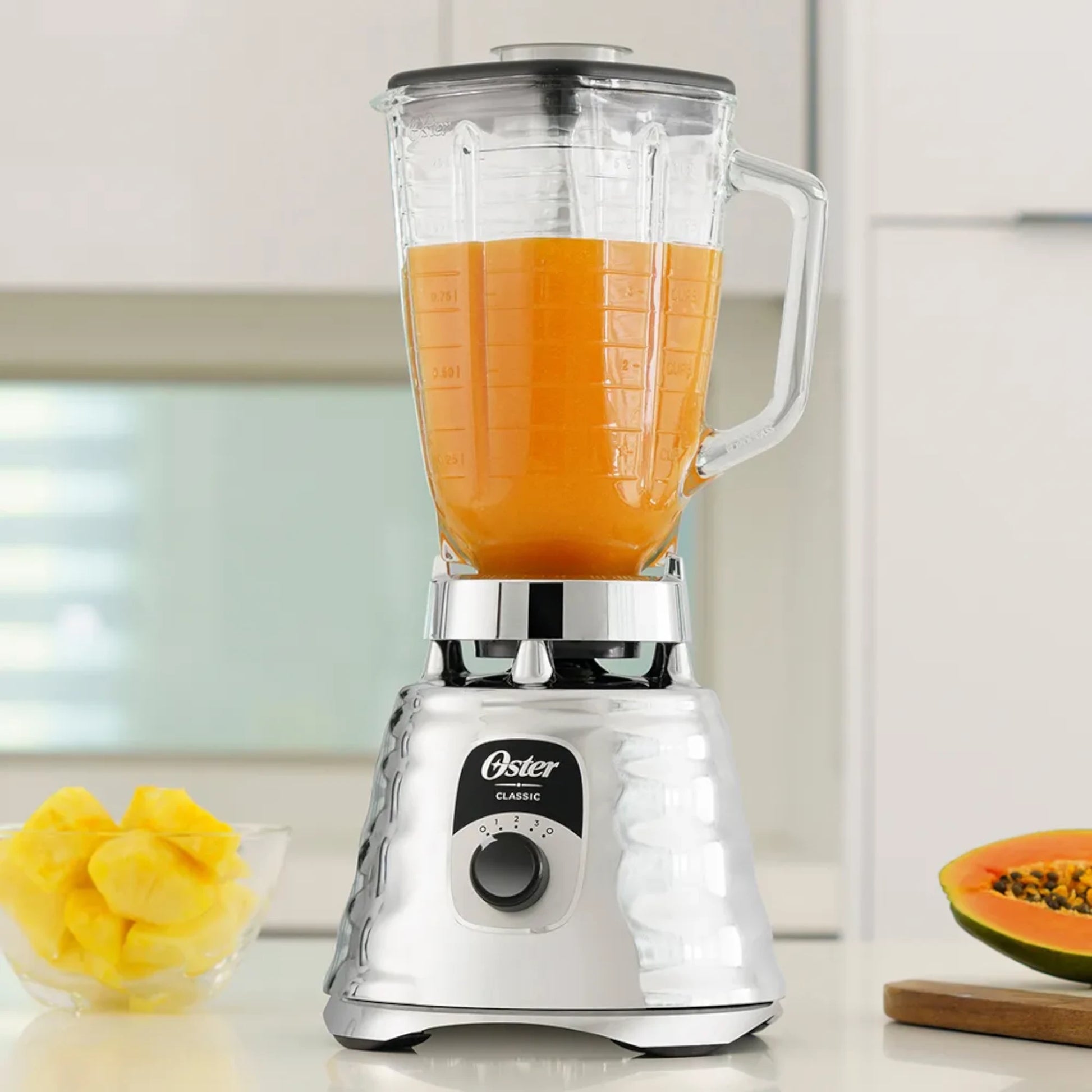 Licuadora clásica Oster cromada BLST4655 con vaso de vidrio lleno de jugo de papaya en cocina moderna.