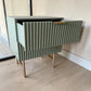 Mesa de noche STUDIO-1061 verde oliva con cajón superior abierto, diseño acanalado vertical, jaladera dorada y patas metálicas.