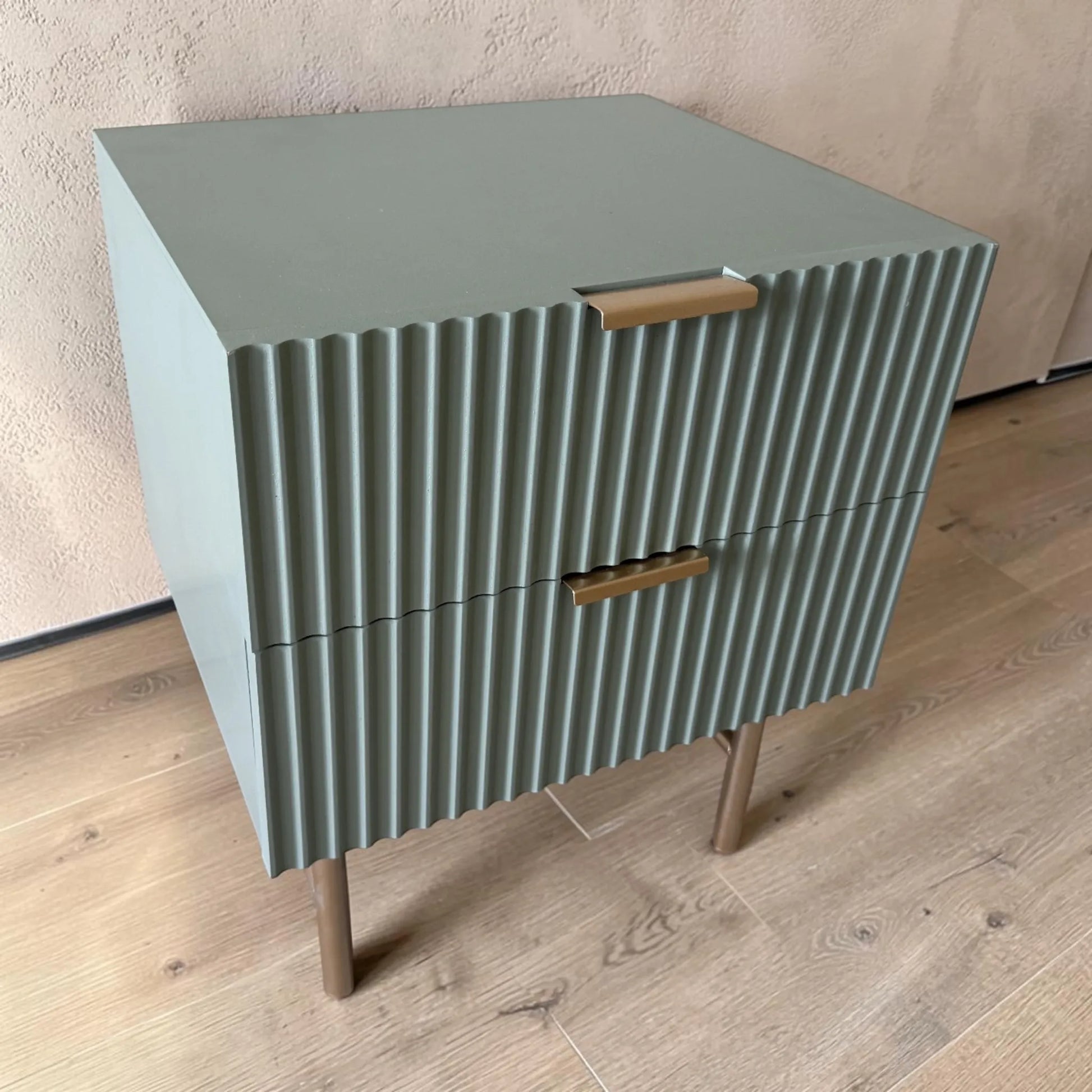 Mesa de noche STUDIO-1061 verde oliva con dos cajones cerrados, acabado acanalado, jaladeras doradas y patas metálicas.