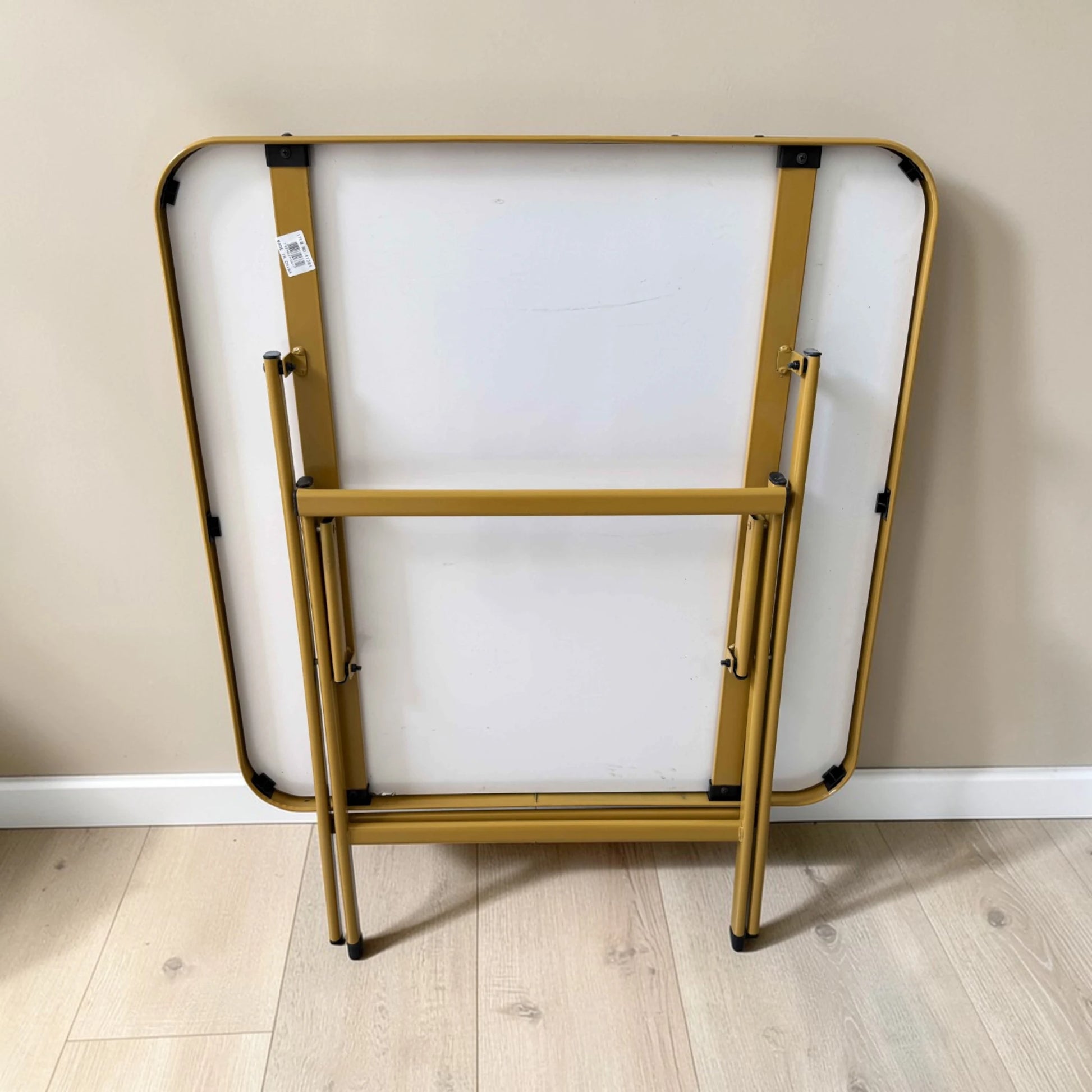 Parte inferior de mesa plegable multiusos cuadrada de 80x80 cm, plegada, con estructura metálica dorada y tablero tipo mármol.