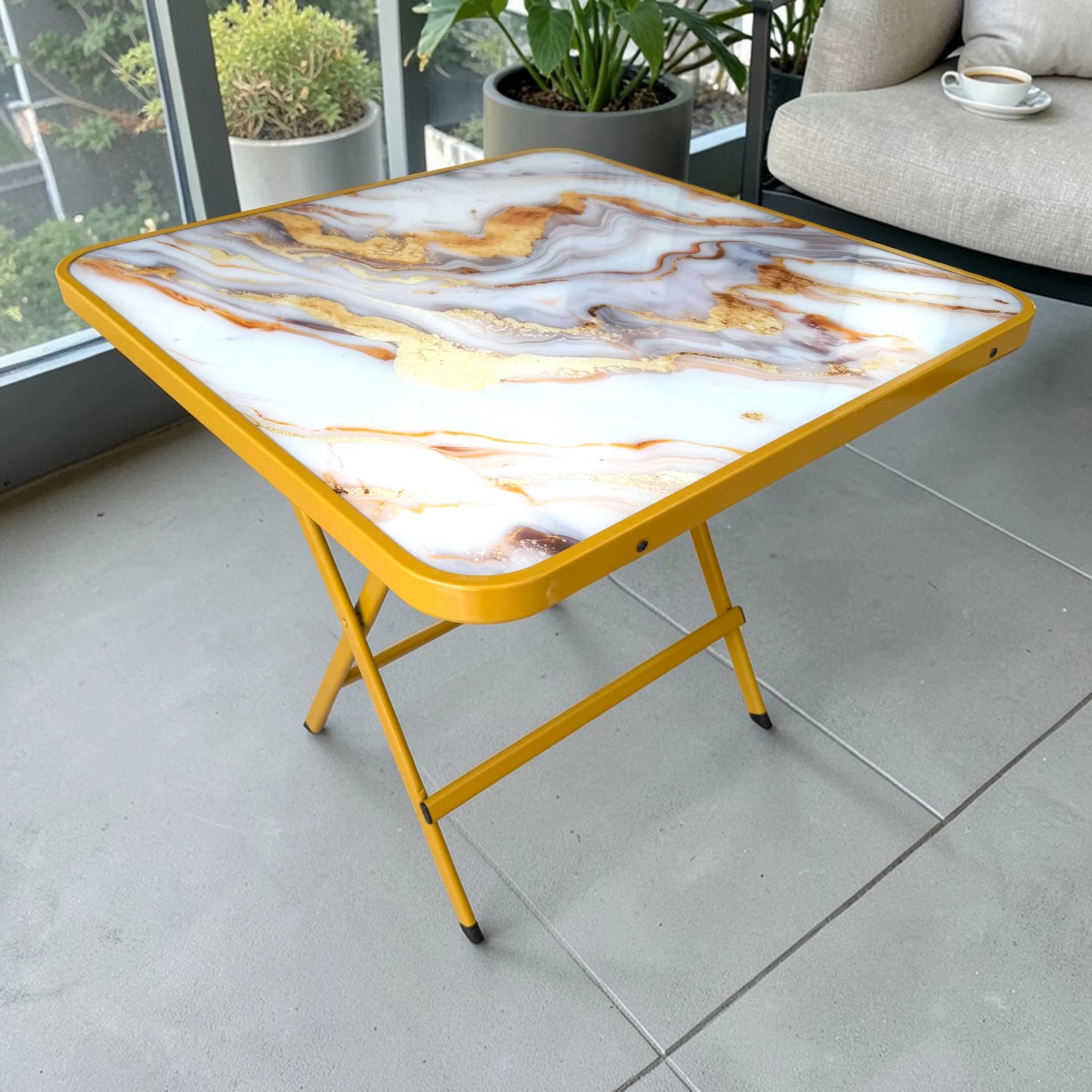 Mesa plegable multiusos cuadrada de 80x80 cm con tablero tipo mármol en tonos blanco, gris y dorado, y estructura metálica dorada, vista frontal en ángulo.