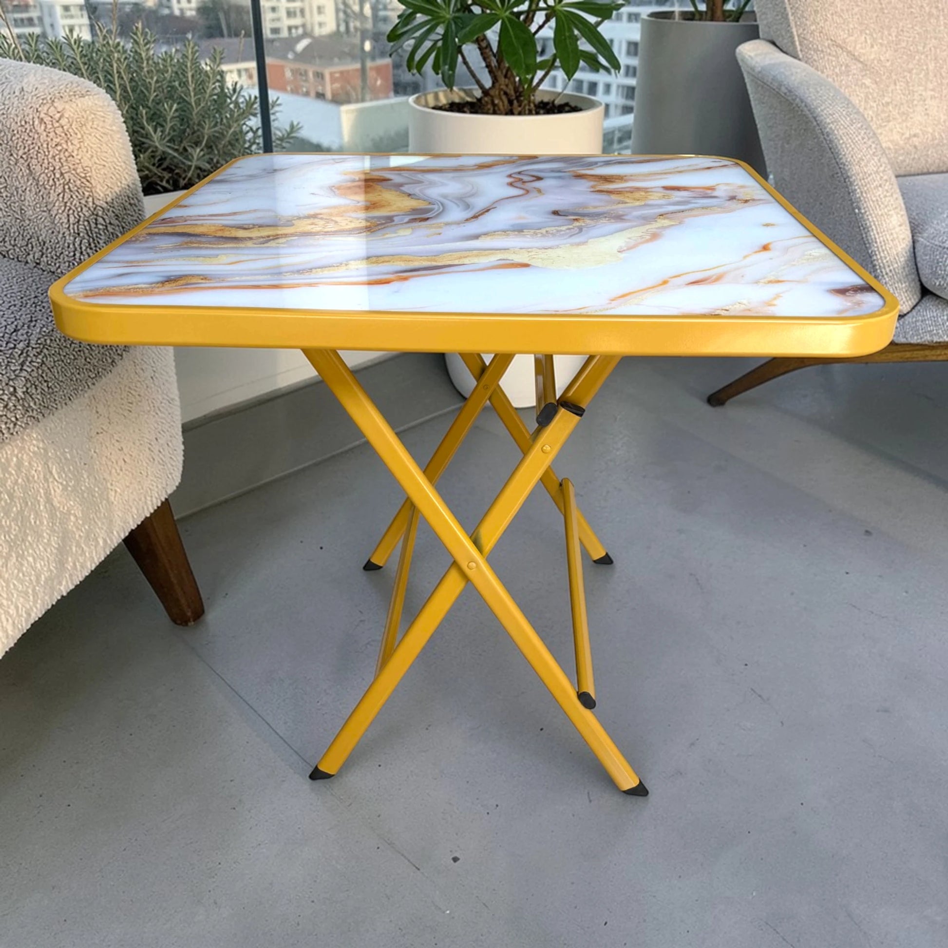Vista lateral de mesa plegable multiusos cuadrada de 80x80 cm con acabado tipo mármol y patas metálicas doradas en forma de cruce.