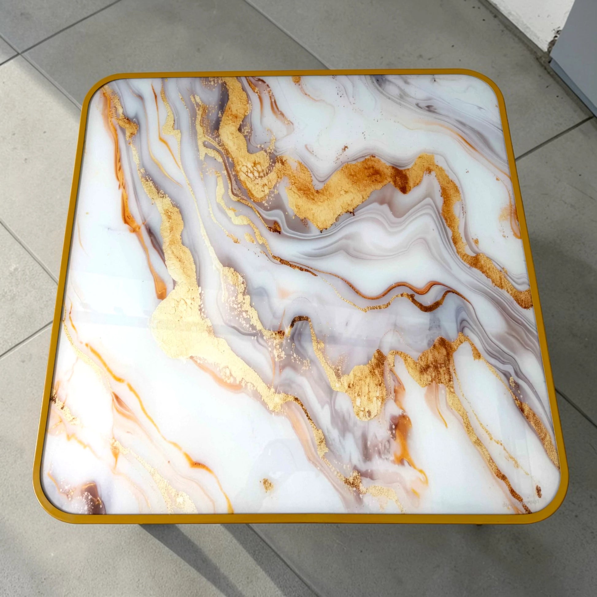 Vista superior de mesa plegable cuadrada de 80x80 cm con tablero tipo mármol en tonos blanco, gris y dorado y borde dorado redondeado.