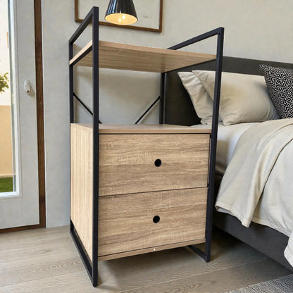 Mesita de noche Flexi Storage Studio de 60 x 58 x 113 cm con estructura metálica negra y paneles color roble, dos gavetas y una repisa superior junto a la cama en un dormitorio moderno.