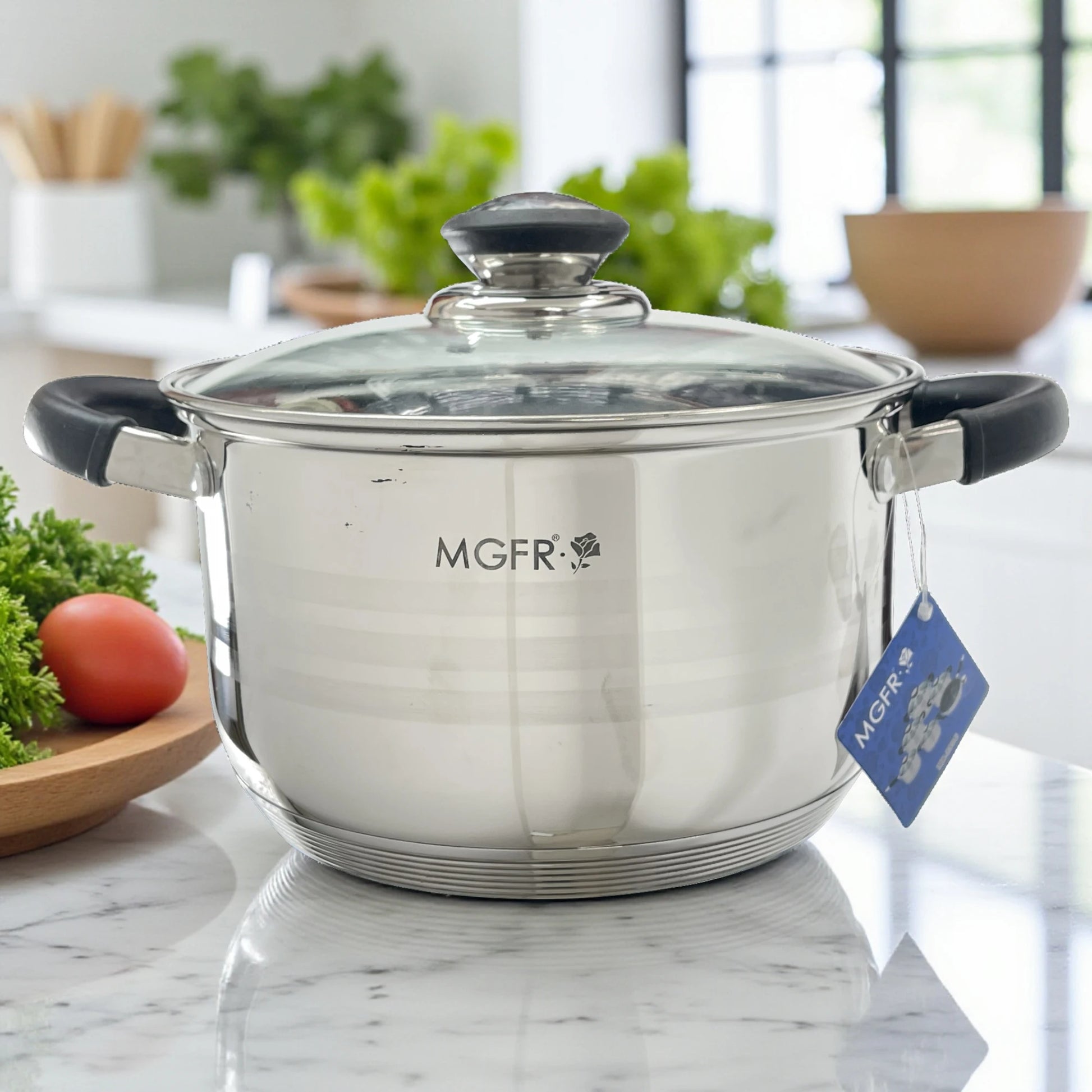 Cacerola grande MGFR MR-290G de 24 x 14.5 cm en acero inoxidable 18/10 con tapa de vidrio y asas térmicas negras; logo MGFR al frente, escena de cocina iluminada.