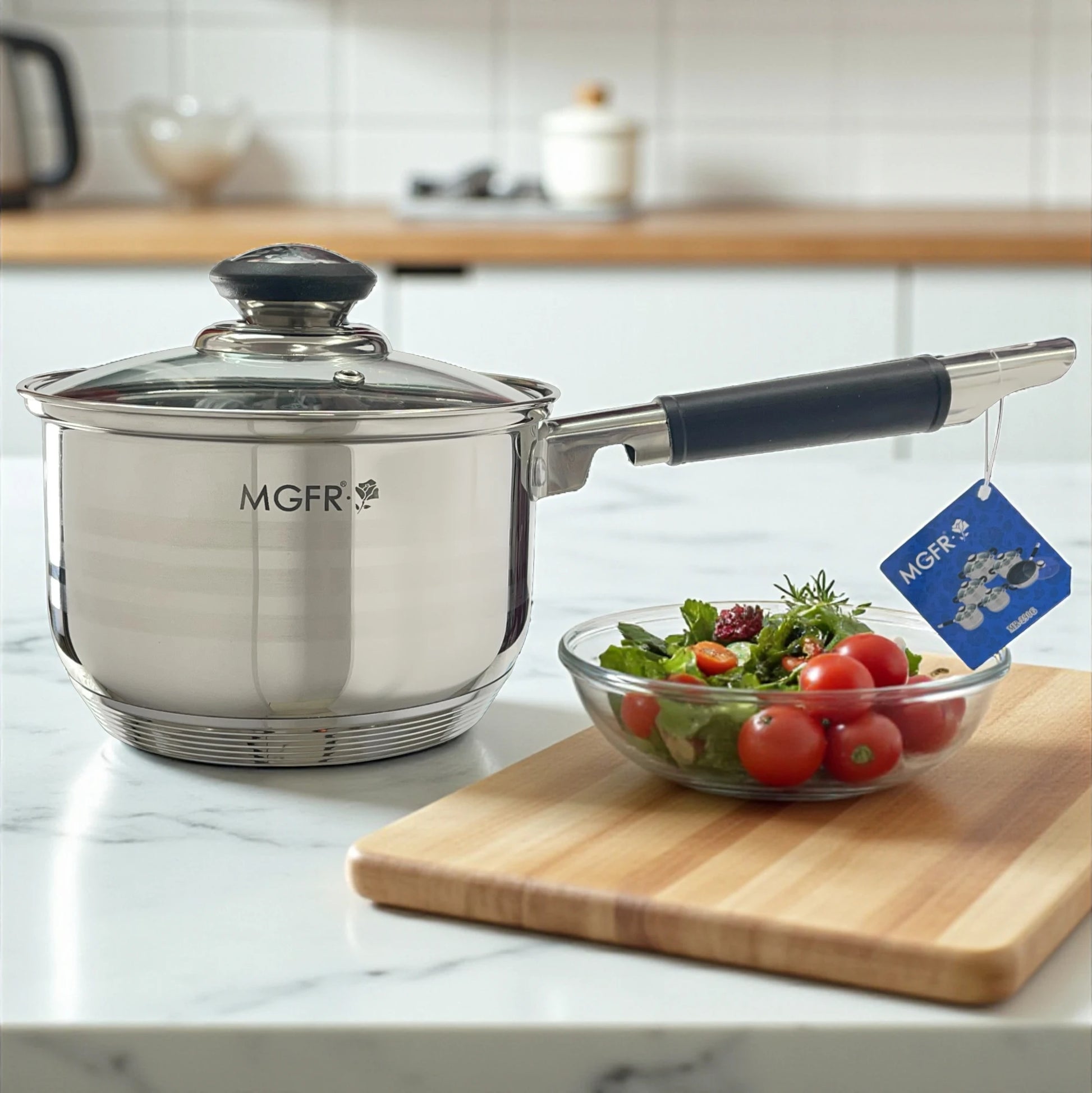 Cazo MGFR 16 x 10.5 cm de acero inoxidable 18/10 con tapa de vidrio y mango largo negro; etiqueta de la marca visible sobre encimera.