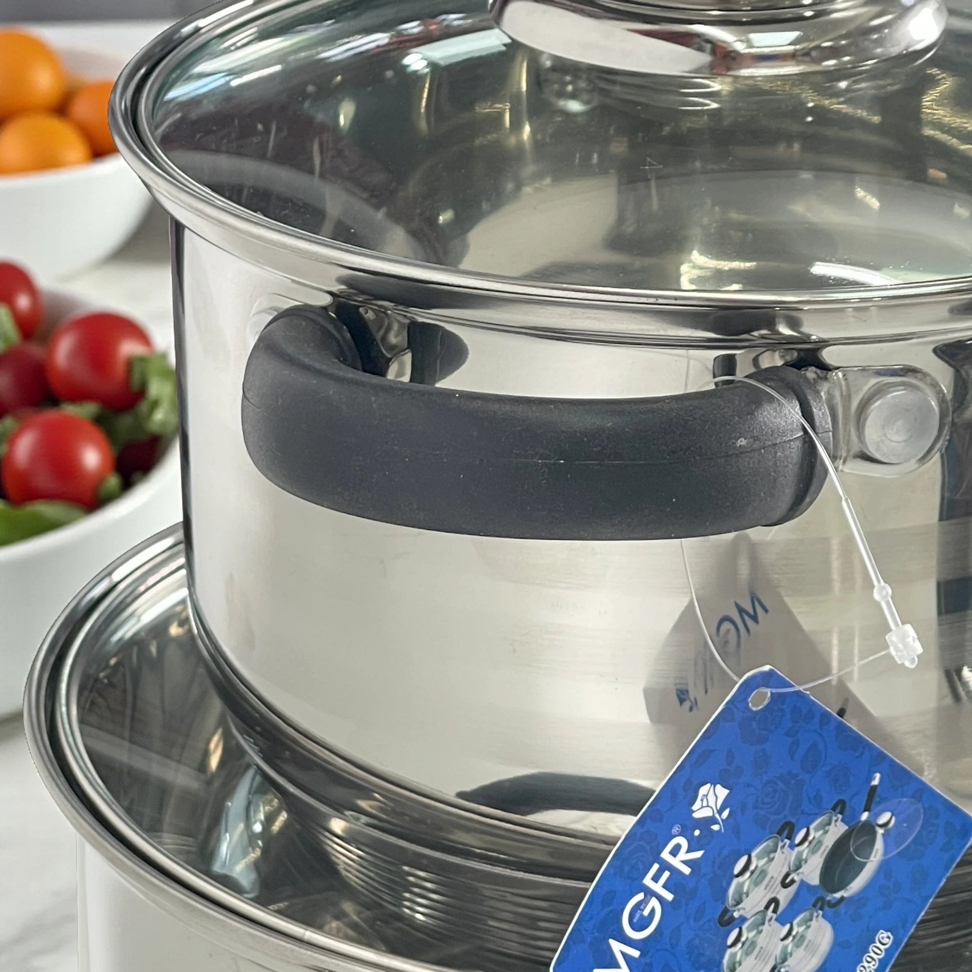 Detalle de asa térmica negra atornillada y borde de tapa de vidrio en olla MGFR MR-290G de acero inoxidable; acabado pulido espejo.