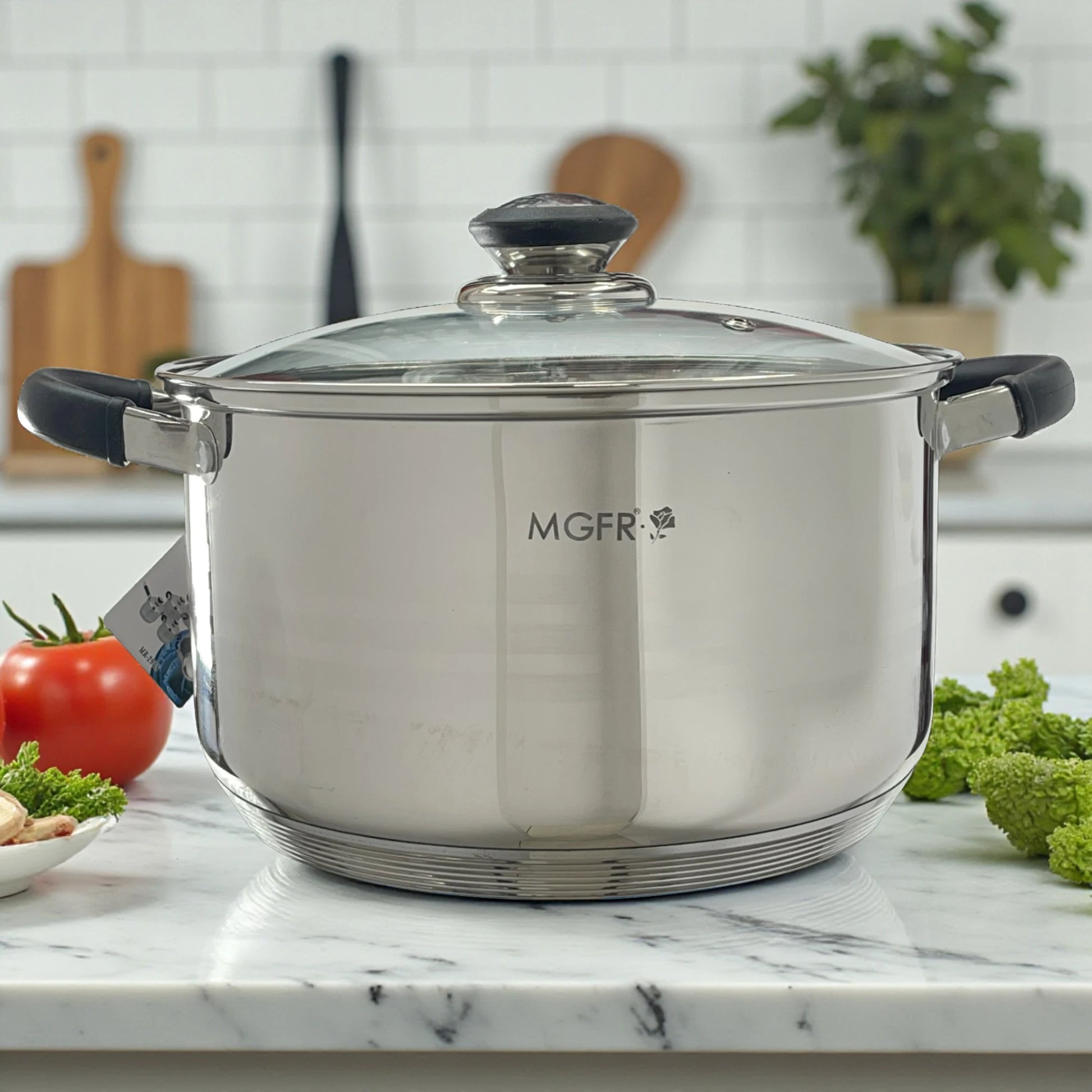 Primer plano de la cacerola MGFR 24 x 14.5 cm en acero inoxidable 18/10 con tapa de vidrio y mangos térmicos negros sobre encimera de mármol.