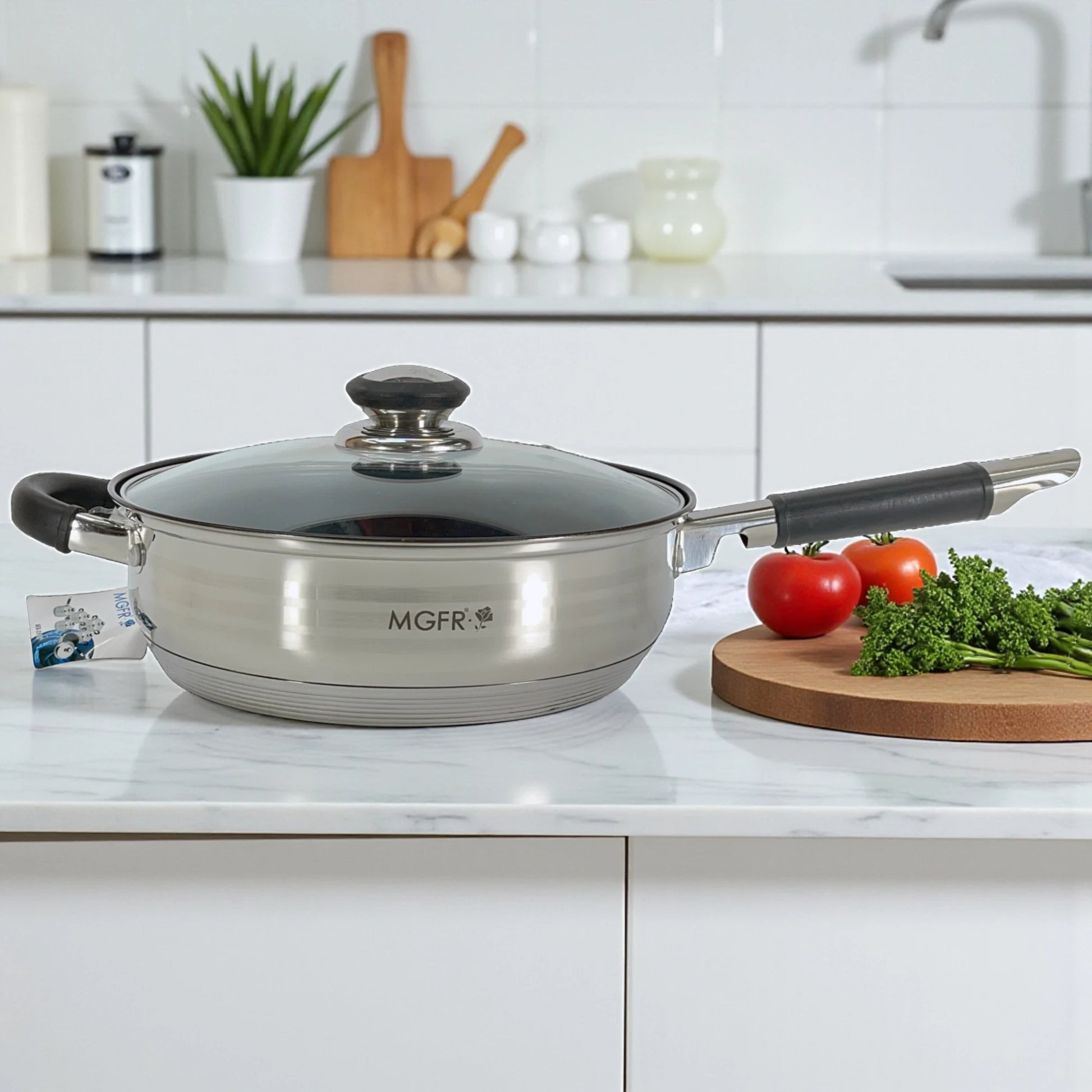 Sartén profunda MGFR MR-290G de 24 x 7.5 cm en acero inoxidable 18/10 con tapa de vidrio, mango largo negro y asa auxiliar sobre encimera blanca.