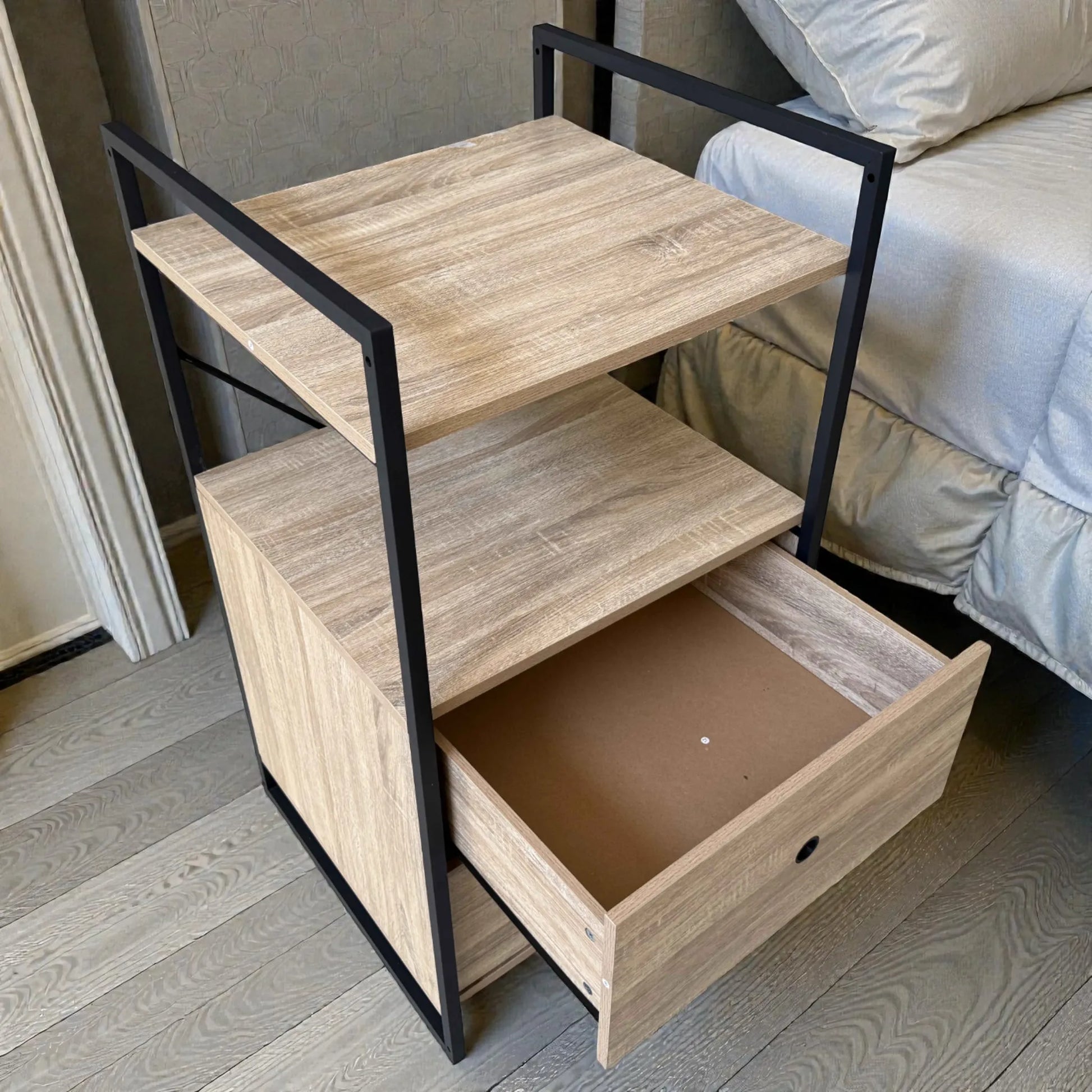 Mueble auxiliar Flexi Storage Studio con estructura metálica negra y paneles roble, visto en ángulo superior, mostrando uno de los cajones inferiores abiertos y la repisa superior, ideal para guardar ropa o accesorios.