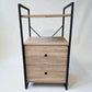 Vista frontal del mueble auxiliar Flexi Storage Studio de 60 x 58 x 113 cm con dos gavetas de melamina color roble, repisa superior y estructura rectangular de metal negro.