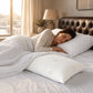 Mujer descansando de lado en una cama con una almohada de bambú Pacific Home blanca visible en primer plano dentro de un dormitorio cálido.